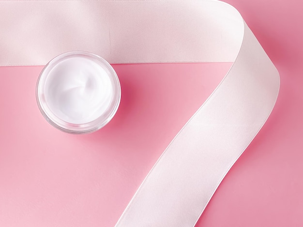 Cosméticos para el cuidado de la piel crema facial crema hidratante tarro y cinta de seda blanca sobre fondo rosa producto de belleza flatlay closeup