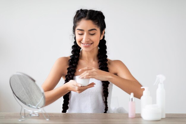 Cosméticos para el cuidado de la piel hermosa mujer india abriendo tarro con crema hidratante en casa