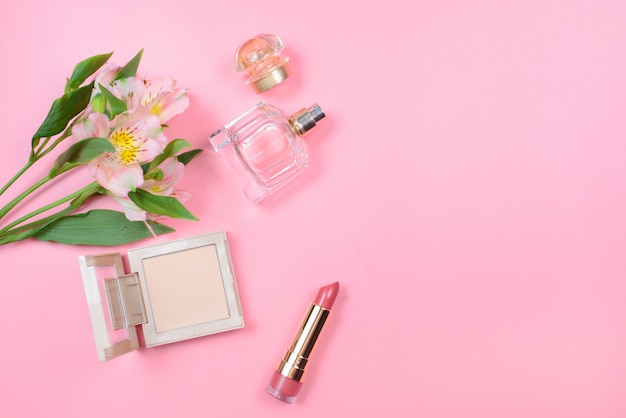 Cosméticos e flores em uma mesa-de-rosa com copyspace