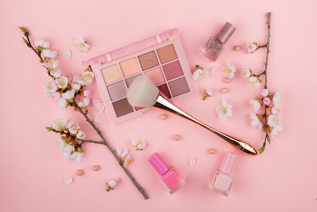 Cosméticos e Sakura ramificam em uma parede rosa. Conceito de beleza, plana leigos.