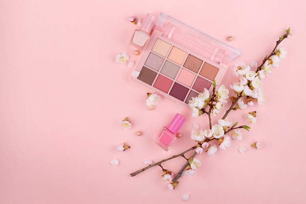 Cosméticos e Sakura ramificam em uma parede rosa. Conceito de beleza, plana leigos.