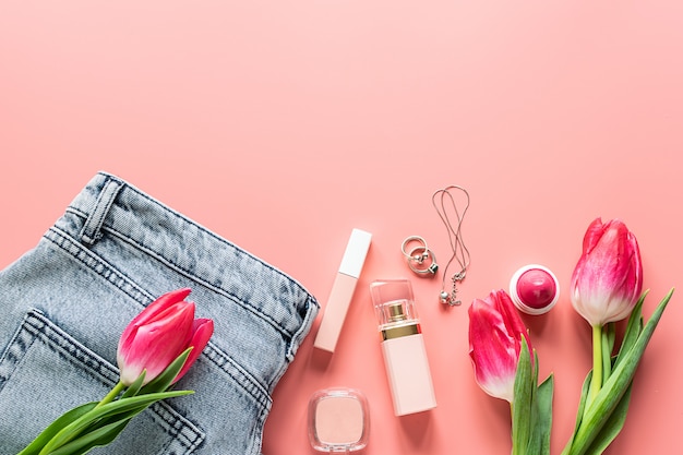 Cosméticos, jeans y accesorios para niñas brillantes sobre fondo rosa moderno