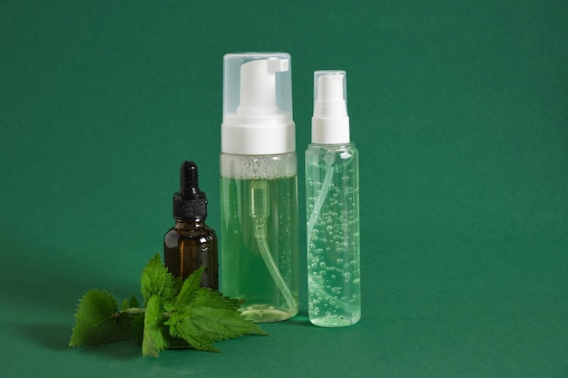 Cosméticos naturais com folhas de urtiga. Loção, creme, xampu em garrafas simuladas, cuidados com a pele e tratamento capilar em fundo verde