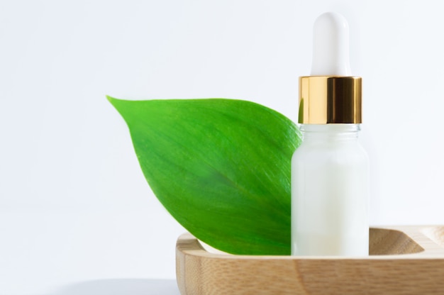 Foto cosméticos naturais: soro com conta-gotas e folhas verdes sobre fundo branco.