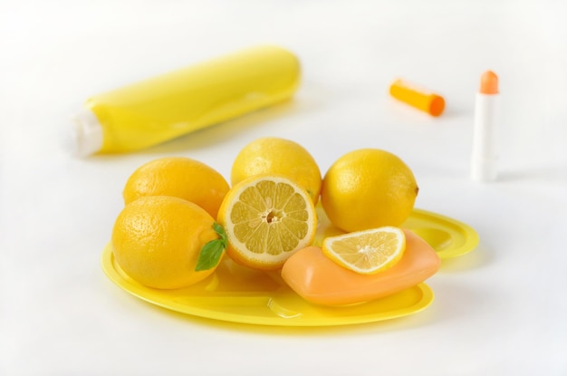 Cosméticos naturales limones y jabón en una paleta sobre un fondo blanco.
