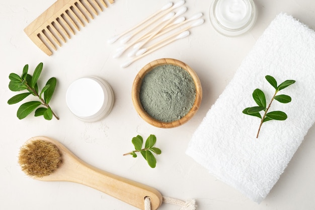 Cosméticos orgánicos para el cuidado de la piel. Cepillo de masaje seco, arcilla cosmética, hisopos de algodón, crema facial, peine de madera, toalla. Vista superior.