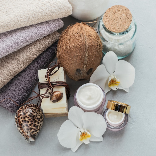 Cosméticos orgánicos con toallas de sal marina de aceite de coco y jabón hecho a mano con flores de orquídeas blancas sobre fondo gris