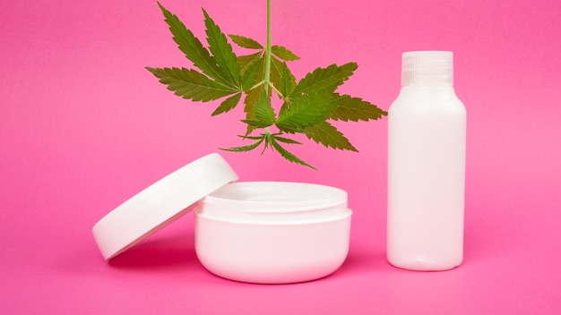 Cosméticos para a pele com extrato de maconha em um fundo rosa, creme rejuvenescedor com folha de cannabis.