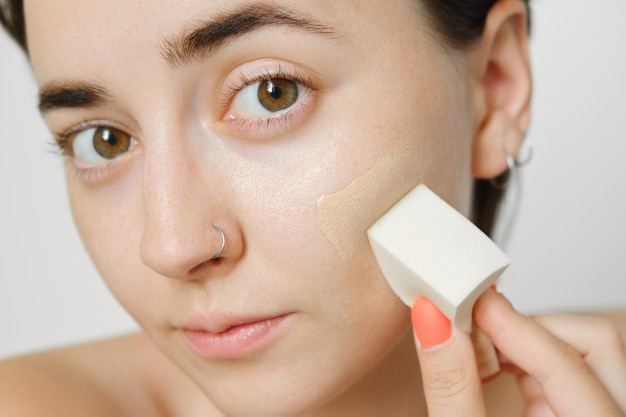 Cosméticos para acne, uma garota aplica uma base tonal com uma esponja para esconder problemas