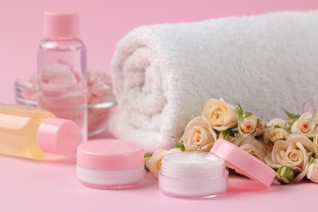 Cosméticos para rosto e corpo em garrafas cor de rosa com rosas frescas em um delicado fundo rosa. creme e loção. spa.