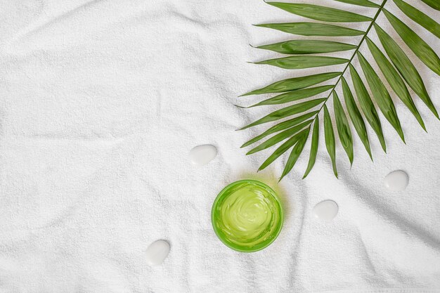 Cosméticos de verano gel hidratante color verde y hoja de palma en la toalla y fondo de piedras blancas para spa