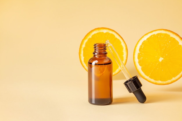 Cosméticos vitamínicos em frasco de vidro contra fatias de laranja em fundo amarelo