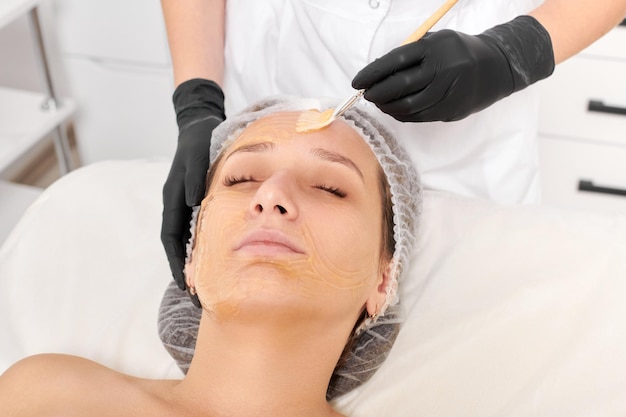 Cosmetóloga aplica máscara de miel en la cara de la mujer para hidratar la piel de la cara en el salón de belleza spa