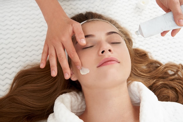 Cosmetóloga aplicando crema en el rostro femenino mujer que tiene un tratamiento facial en el salón de spa