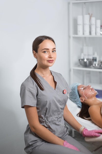 Cosmetóloga aplicando crema en el rostro hermoso de una mujer con un cepillo cosmetólogo Luz de lámpara enfocada en la cara