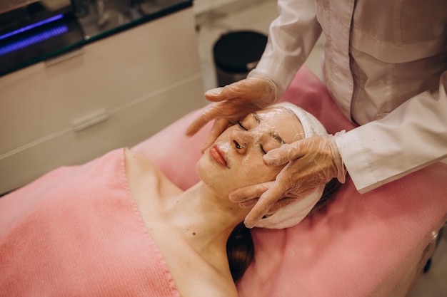 Cosmetóloga aplicando máscara en la cara de la mujer en el salón de belleza