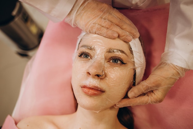 Cosmetóloga aplicando máscara en la cara de la mujer en el salón de belleza