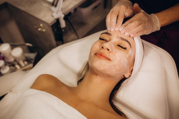 Cosmetóloga aplicando máscara en la cara de la mujer en la vista superior del salón de spa Espacio para texto