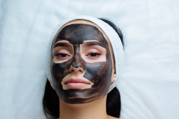 Cosmetóloga aplicando máscara negra en la cara de una mujer bonita con guantes negros mujer hermosa en el spa ...