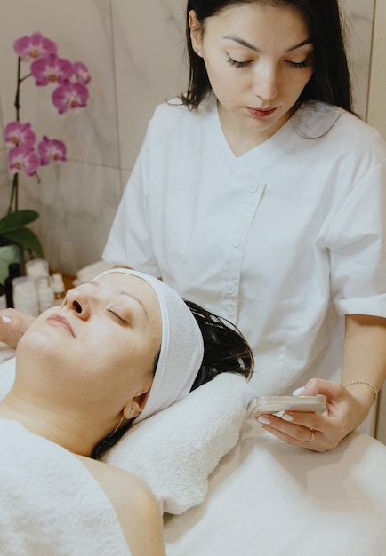 Cosmetóloga com um telemóvel e um paciente numa mesa de massagem