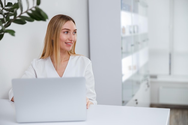 Cosmetóloga femenina alegre usando laptop en salón de belleza