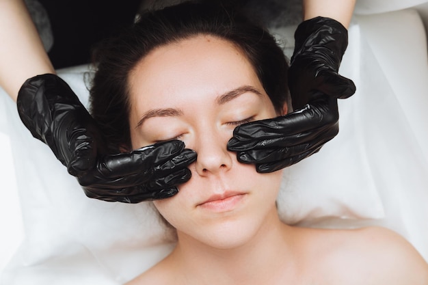 Una cosmetóloga hace un masaje facial cosmético para la cara relajada de una mujer joven en un spa de belleza Masaje para el cuidado facial concepto de cosmetología para el cuidado de la piel