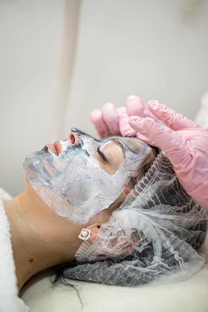 Cosmetóloga haciendo un masaje de elevación en la cara con una máscara facial rejuvenecedora para su clienta