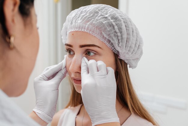 La cosmetóloga limpia la cara del paciente después del procedimiento de llenado del surco nasolagrimal y mesoterapia alrededor de los ojos para una joven hermosa Cosmetología moderna