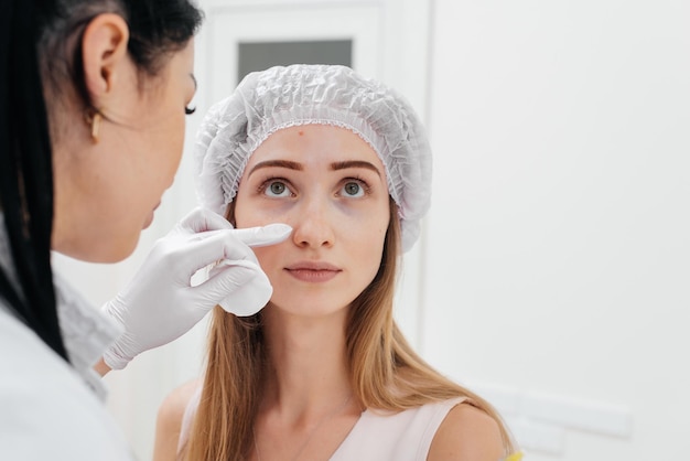 La cosmetóloga limpia la cara de los pacientes después del procedimiento de llenado del surco nasolagrimal y mesoterapia alrededor de los ojos para una joven hermosa Cosmetología moderna