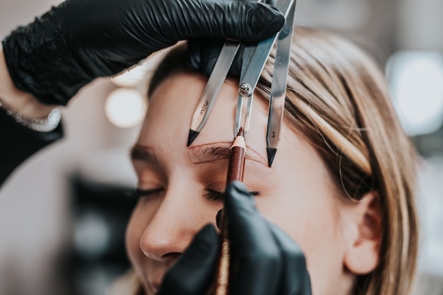 La cosmetóloga mide las proporciones de las cejas con la regla. Flujo de trabajo de micropigmentación en un salón de belleza.