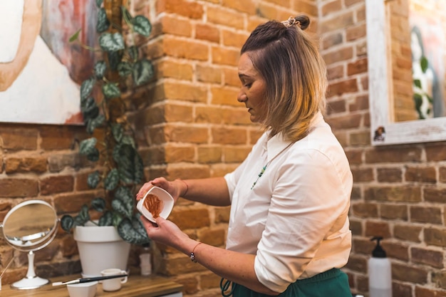 Cosmetóloga preparando una máscara de barro en un cuenco para su cliente en el salón de cosmetología