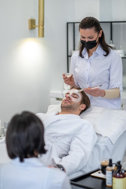 Cosmetóloga profesional aplicando mascarilla hidratante en el área de los ojos del hombre