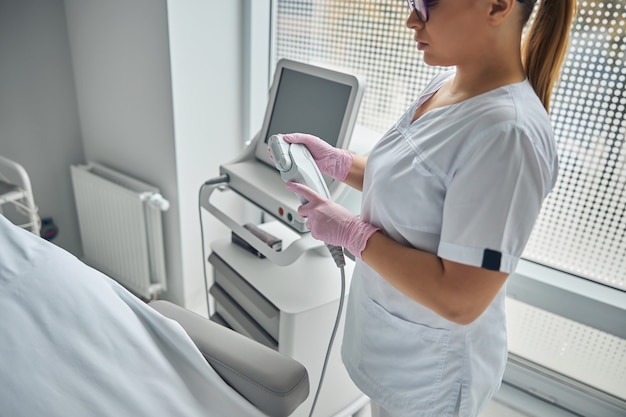 Cosmetóloga profesional en guantes estériles con máquina de depilación láser y rejuvenecimiento de la piel en salón de belleza