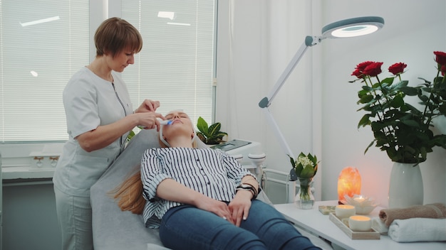Cosmetóloga profesional haciendo peeling de cavitación en la cara de una mujer joven