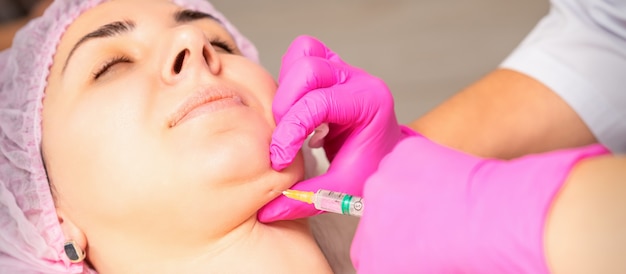 La cosmetóloga realiza una inyección lipolítica en el mentón de una mujer joven contra la papada