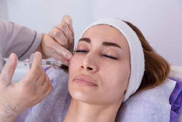 Cosmetóloga realiza inyecciones de relleno antiarrugas rejuvenecedoras con relleno de ácido hialurónico en la cara de una mujer Cosmetología estética femenina en un salón de belleza