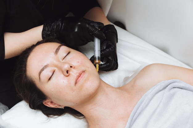 Una cosmetóloga realiza un levantamiento de plasma en la cara de una mujer hermosa en un salón de belleza El concepto de cosmetología