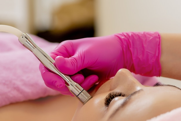La cosmetóloga realiza el procedimiento Microdermoabrasión de la piel facial de una bella y joven mujer en un salón de belleza.Cosmetología y cuidado profesional de la piel.
