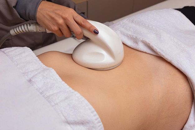 Cosmetología de hardware. Cuidado del cuerpo. Tratamiento de spa. Tratamiento de contorno corporal con cavitación ultrasónica. Una mujer recibe terapia anticelulítica y antigrasa en un salón de belleza.