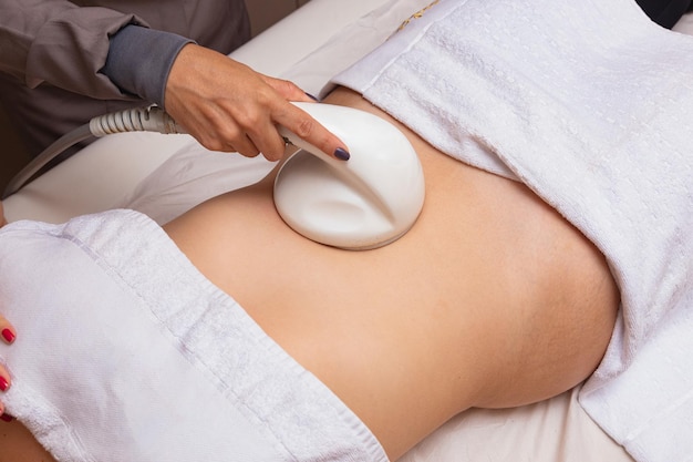 Cosmetología de hardware. Cuidado del cuerpo. Tratamiento de spa. Tratamiento de contorno corporal con cavitación ultrasónica. Una mujer recibe terapia anticelulítica y antigrasa en un salón de belleza.