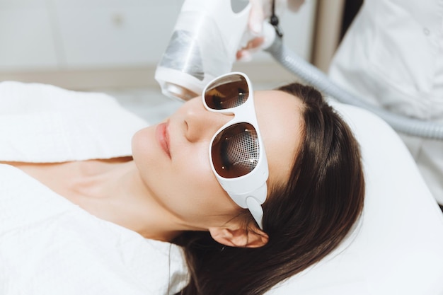 Cosmetologia linda mulher recebendo procedimento de depilação a laser no salão de beleza closeup das mãos de uma esteticista fazendo procedimentos cosméticos para o rosto de uma mulher em um salão de spa