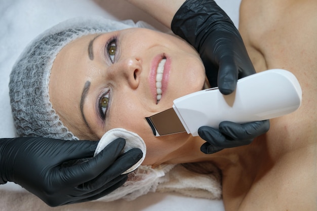 Cosmetología, mujer madura recibiendo limpieza facial con un dispositivo ultrasónico