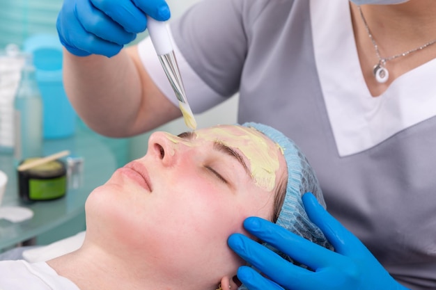 Cosmetologista aplica máscara de alginato com espátula no rosto da mulher