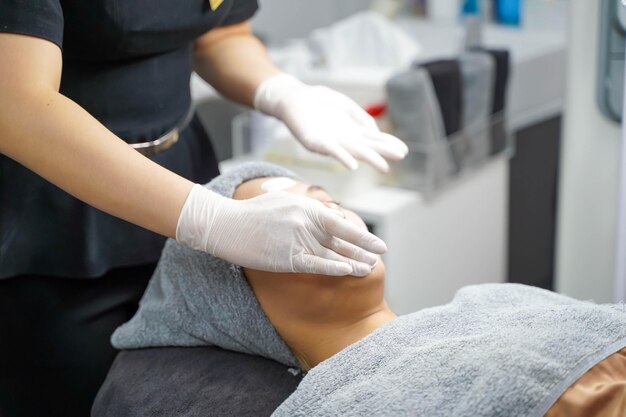 cosmetologista aplicando creme de máscara facial branca suave e massagem em mulher de beleza fazendo spa de rosto