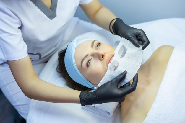 Foto cosmetologista aplicando máscara facial no rosto de uma mulher em um salão de spa