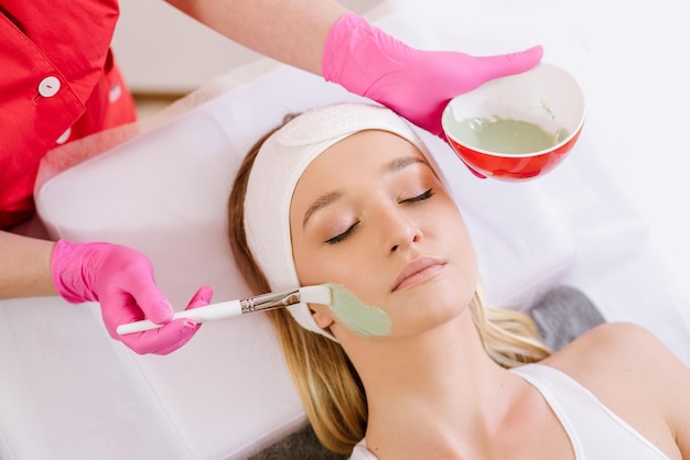 Cosmetologista aplicando máscara no rosto da mulher no salão spa