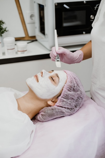 Cosmetologista aplicando máscara no rosto do cliente em salão de spa jovem recebendo cuidados faciais