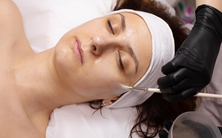 Cosmetologista aplicando produto de peeling químico no rosto do cliente no salão