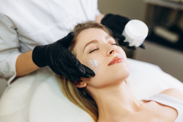 Cosmetologista aplicando vitaminas essenciais de essência de creme no rosto para melhorar a pele do cliente.