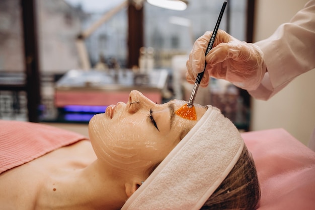 Cosmetologista aplicar máscara no rosto da mulher no salão de beleza